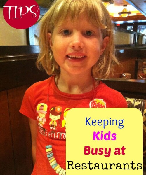 A smiling child with blond hair stands in a restaurant wearing a red shirt and a candy necklace. An overlay text box reads "Keeping Kids Busy at Restaurants." Another smaller red circle in the top left corner has the word "TIPS" in white, making it easier than ever for keeping kids busy at restaurants.