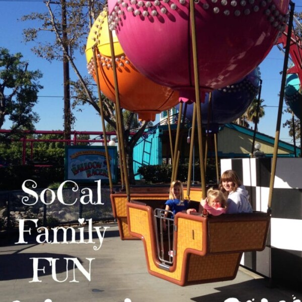 Three children are seated in an orange and brown hot air balloon-themed ride at Adventure City amusement park. The background shows trees and other amusement park structures. Text on the image reads "SoCal Family FUN - Adventure City.