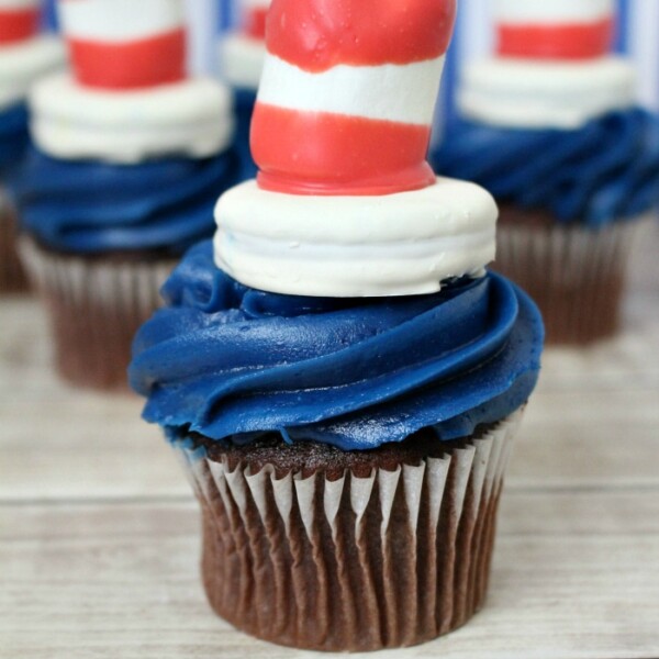 Chocolate cupcakes with blue frosting, topped with candy shaped like red and white striped hats, make a whimsical treat perfect for a Doctor Seuss birthday celebration.