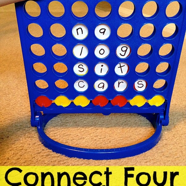 A hand is placing a lettered disk into a Connect Four game. The disks in the game spell out various words. The blue game apparatus features yellow and red disks. At the bottom of the image, the text "Connect Four Spelling" highlights this fun twist on classic spelling games.