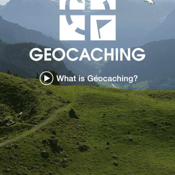 A smartphone screen displays a geocaching app with a mountain landscape in the background. The screen shows options to "Connect with Facebook" or "Connect with Geocaching." A "What is Geocaching?" video button is also visible, inviting users to dive into the adventurous world of geocaching.