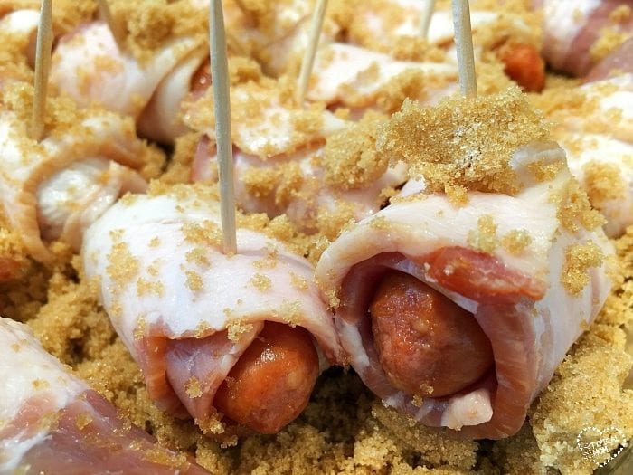 Close-up of bacon-wrapped hot dogs, expertly secured with toothpicks and generously sprinkled with brown sugar.