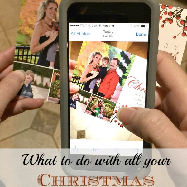 A person is holding a smartphone displaying a photo of a holiday card with family pictures. Behind the phone, the person is holding two physical holiday cards. Text on the image reads, "Wondering what to do with Christmas cards?