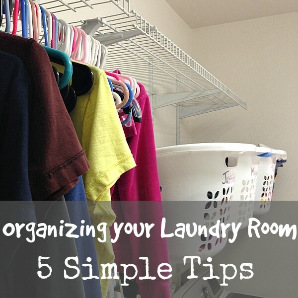 A laundry room with clothes hanging on hangers, a plastic laundry basket, and a detergent bottle on the washing machine. Text overlay reads: Organize Your Laundry Room: 5 Simple Tips for a Tidy Space.