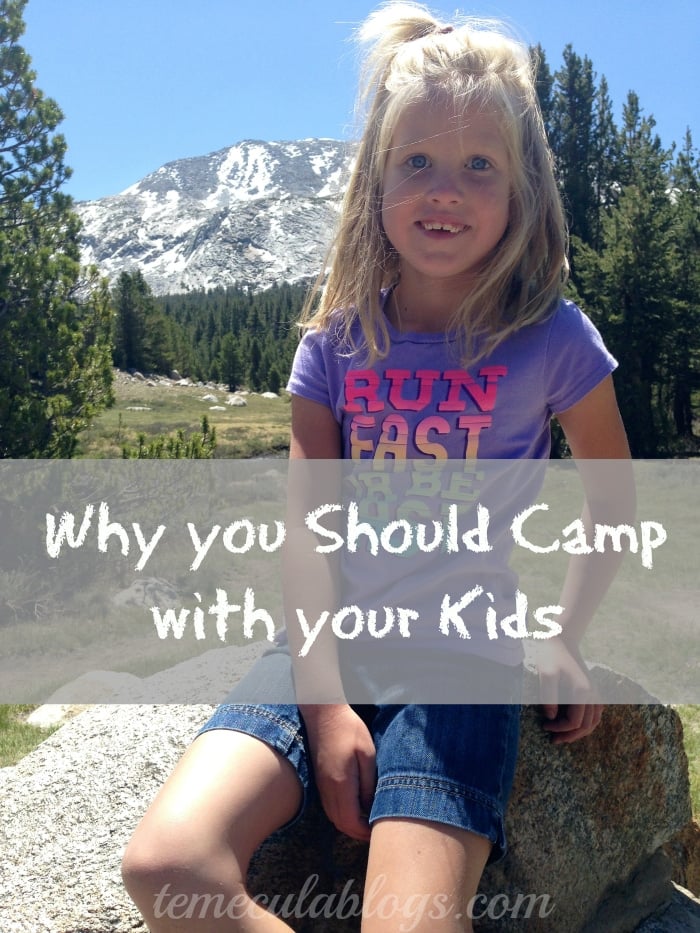 A young girl with blonde hair wearing a purple t-shirt and denim shorts sits on a rock in a mountainous area. Text over the image reads, 