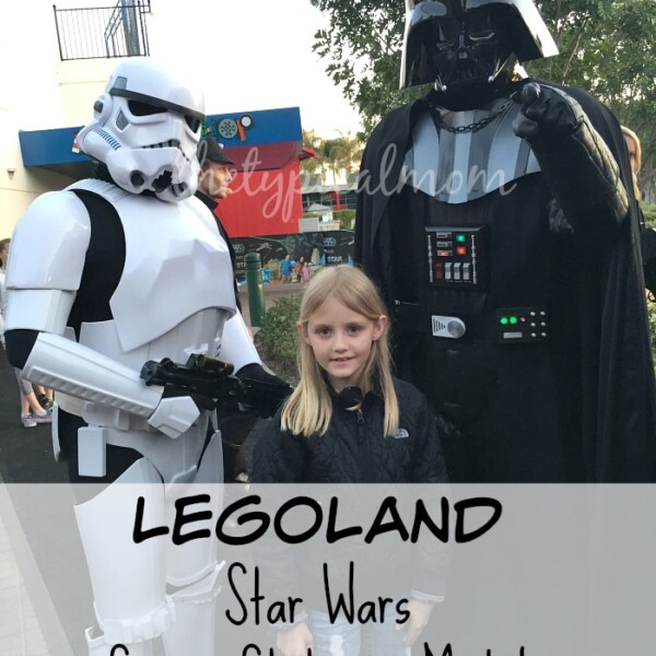 A child stands between individuals dressed as a Stormtrooper and Darth Vader from Star Wars. The background features part of an amusement park. Overlaid text reads "LEGOLAND Star Wars Space Station & Model," celebrating LEGO Star Wars Days.