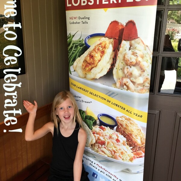 A child sits smiling next to a vibrant Lobsterfest at Red Lobster banner adorned with tempting images of seafood dishes. The text joyously declares, "Time to Celebrate!