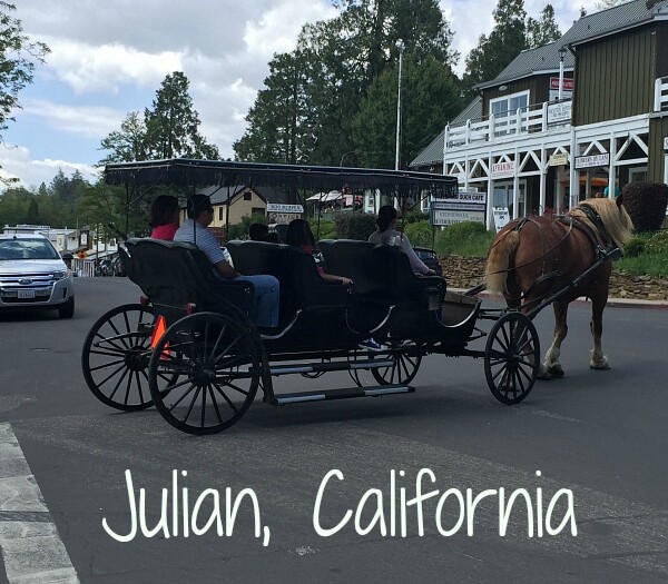 In the heart of Julian, California, a horse-drawn carriage glides along the street, carrying passengers past charming buildings and lush trees.