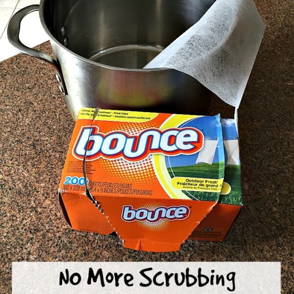 A kitchen pot with a dryer sheet inside sits beside an open box of Bounce on the countertop. Handwritten text below reads, No More Scrubbing—Discover How to Clean a Burnt Pot without Baking Soda effortlessly!