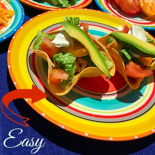 Colorful plates with taco salad bowls brimming with lettuce, tomato, cheese, and avocado slices. Text reads Easy Taco Cup Tutorial.