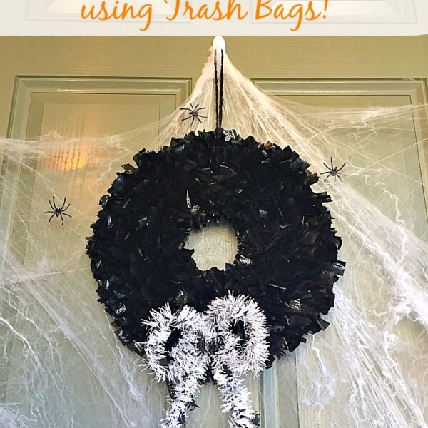 A festive Halloween wreath crafted from black trash bags, adorned with a white tinsel bow, hangs mysteriously on the door amidst encircling fake cobwebs and plastic spiders.