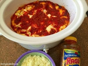 Easy crockpot lasagna recipe featuring a rich tomato sauce and gooey cheese. A jar of Ragu sauce and a bowl of shredded cheese rest beside the slow cooker, ready to create this deliciously simple dish.