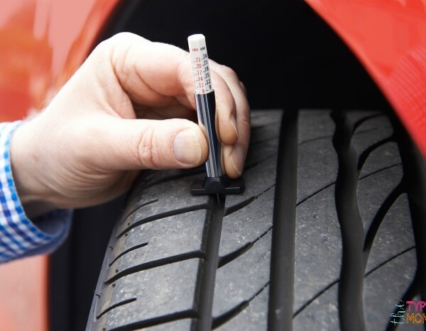 A person checks the tread depth of a car tire using a tread depth gauge, mindful of where to go when you need new tires to ensure safety and reliability.