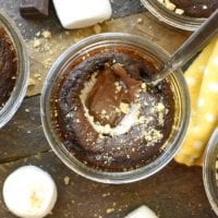 S'mores in a jar: glass jars filled with smores lava cake, topped with melted chocolate and marshmallows, all presented on a rustic wooden surface.