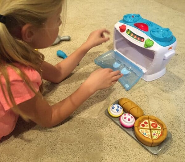 A child joyfully interacts with LeapFrog's Number Lovin' Oven, surrounded by delightful pretend food on a soft, carpeted floor.