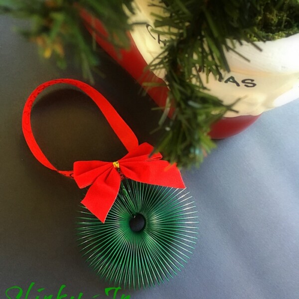 A green Slinky Jr. ornament with a red bow graces the Christmas tree, echoing the festive charm of a Slinky wreath ornament. The text "Slinky Jr. Ornament" is elegantly displayed at the bottom of the image.