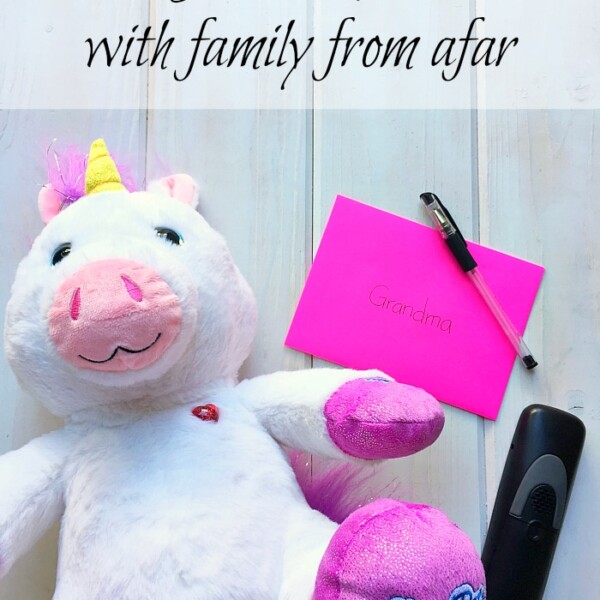 A plush unicorn, a pink envelope labeled Grandma, a pen, and a black device are arranged on the table. This setup is perfect for helping kids stay connected with family from afar.