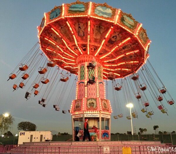 At the OC Winter Fest, the illuminated swing ride glows against a twilight sky, its empty swings gently swaying from the rotating canopy.