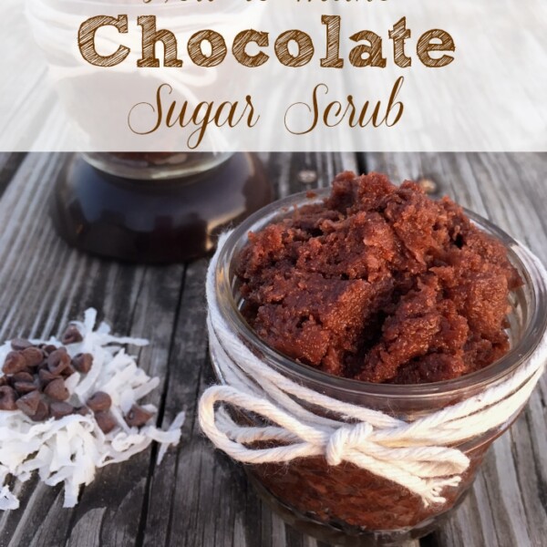 Jar of chocolate sugar scrub with twine, placed on a wooden surface. Shredded coconut and chocolate chips are scattered nearby. Text overlay reads, How to make a sugar body scrub that leaves your skin feeling silky smooth.