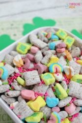 A colorful cereal mix with marshmallows, sprinkles, and square cereal pieces in a white bowl is reminiscent of a playful twist on a classic Peanut Butter Muddy Buddies recipe.
