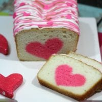 A loaf of sliced surprise cake with white icing and a pink zigzag pattern, featuring a delightful pink heart shape in the center of each slice.