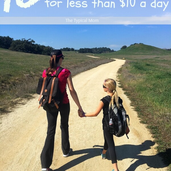 An adult and child, both with backpacks, stroll hand in hand along a dirt path through a grassy landscape. Text above reads, 10 activities to do with kids for less than $10 a day.