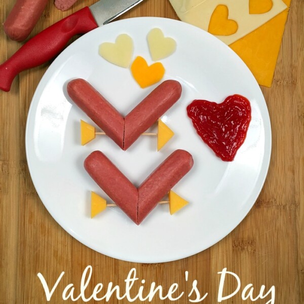 Plate with heart-shaped hot dogs, cheese slices, and ketchup. Knife and ingredients on a wooden board. A perfect Valentine dinner idea for memorable moments. Valentines Day Heart Dogs text at the bottom.