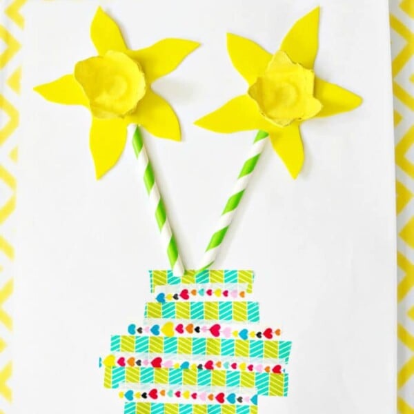 Create a charming Mother's Day craft for kids with a vase featuring two yellow daffodils crafted from paper and straws, all set against a vibrant yellow chevron background.