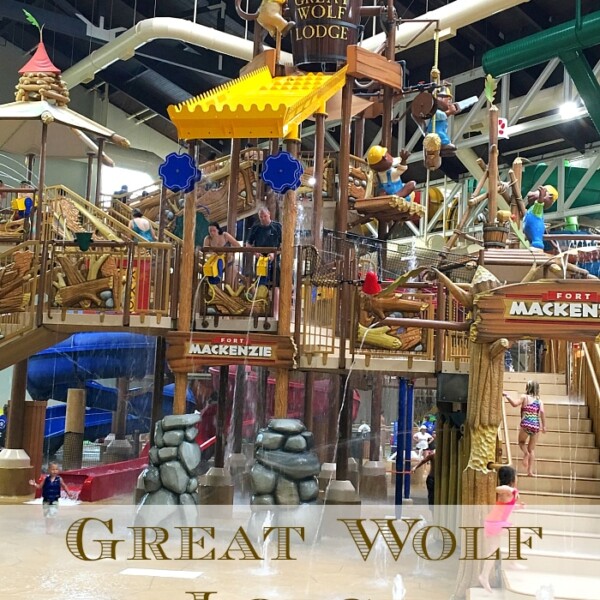 The vibrant indoor water park at Great Wolf Lodge Southern California buzzes with excitement, featuring a wooden structure adorned with slides and water features. Families delight in the attractions beneath the large "Great Wolf Lodge" sign, creating a bright and colorful atmosphere.