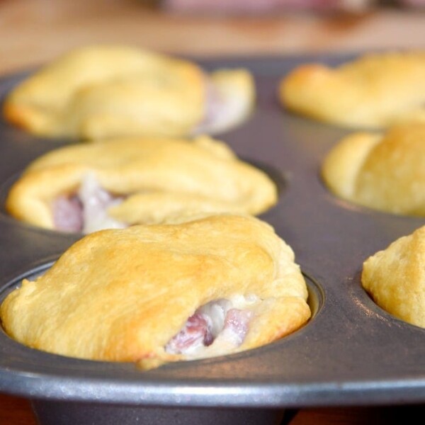 Golden brown ham turnovers, the perfect leftover ham recipe, nestle in a muffin tin on a rustic wooden table.