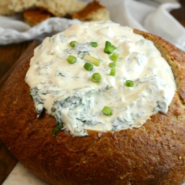 A round loaf of bread is hollowed out and generously filled with cold spinach dip, then topped with chopped green onions for a refreshing twist.