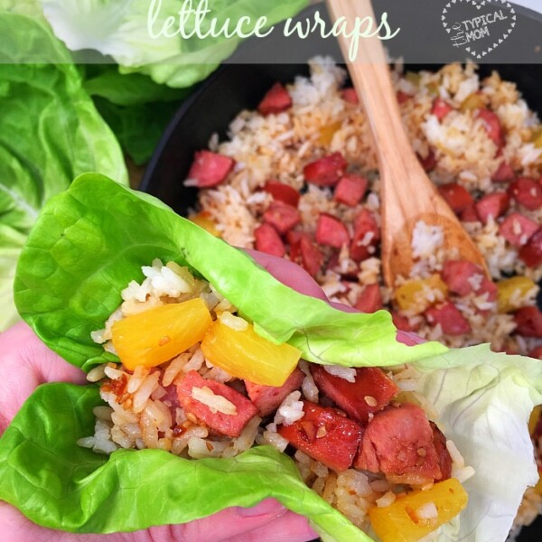 A hand holds a vibrant Hawaiian lettuce wrap filled with rice, diced sausage, and pineapple, while more of the flavorful filling awaits in a bowl in the background.