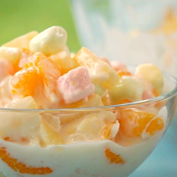 Bowl of creamy, easy ambrosia salad with fruit and pastel marshmallows. Text at the top reads Easy Ambrosia Recipe.