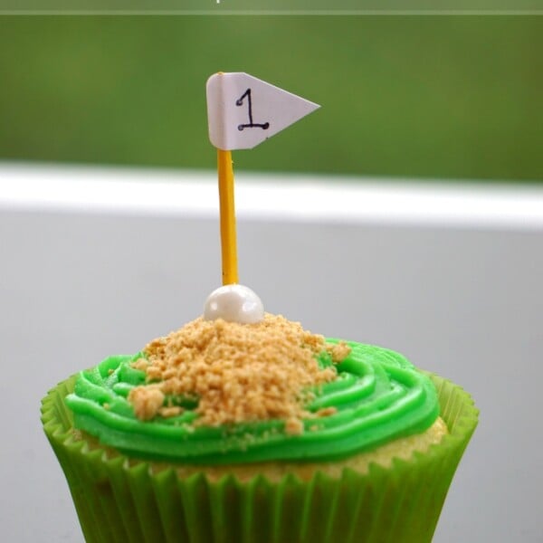 Green cupcake adorned with a golf theme, featuring a small flag marked with the number one. Text above reads, perfect Fathers Day cupcakes.