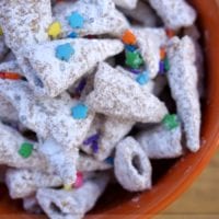 A bowl brimming with powder-coated cereal pieces, reminiscent of unicorn horns, is adorned with vibrant star and round sprinkles. The text on the image proudly proclaims "Unicorn Horn Muddy Buddies.