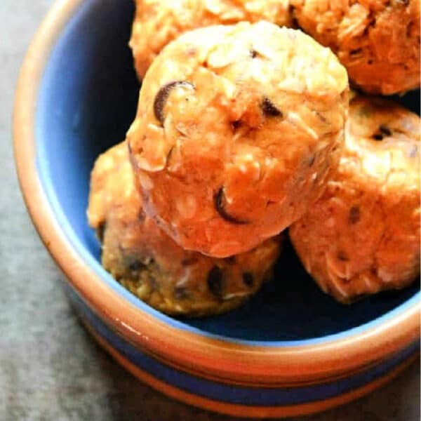 A blue bowl filled with round oatmeal and chocolate chip energy bites, made using a simple energy ball recipe, sits on a dark surface.