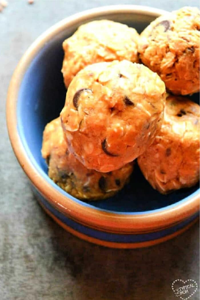 A blue bowl filled with round oatmeal and chocolate chip energy bites, made using a simple energy ball recipe, sits on a dark surface.