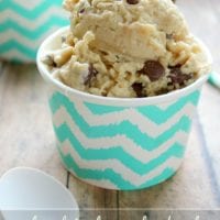 A cup of chocolate chip cookie dough frozen yogurt sits on a wooden table, its zigzag pattern cup catching the eye—a tempting treat perfect for those curious about how to make frozen yogurt at home.