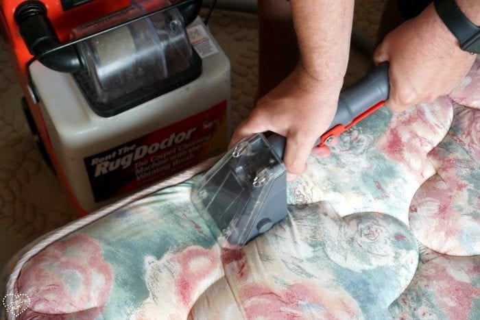 A person follows their house cleaning checklist, using a carpet cleaning machine to tackle a floral-patterned mattress.