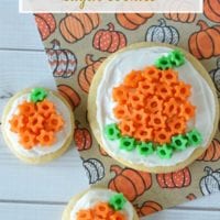 Three delightful pumpkin sugar cookies adorned with vibrant orange and green frosting rest on a charming pumpkin-patterned napkin.