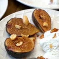 Grilled figs with nuts and a scoop of vanilla ice cream on a white plate, reminiscent of learning how to bake figs in the oven for that perfect caramelized flavor.