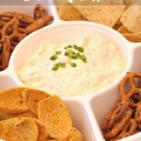 A divided tray showcasing the most incredible beer cheese dip recipe is adorned with chopped green onions and surrounded by a variety of pretzels, tortilla chips, and corn chips.