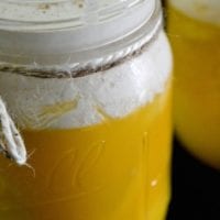 A glass jar brimming with creamy yellow pudding evokes the delightful flavor of an orange creamsicle drink, topped with a swirl of whipped cream and a delicate sprinkle of cinnamon.