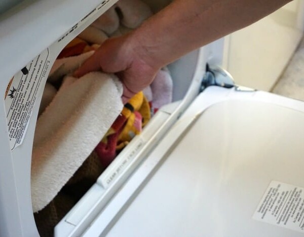 A hand carefully places towels into a front-loading washing machine, illustrating one of the ways to conserve energy.