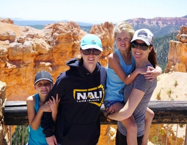 Four friends posing in front of the breathtaking Bryce Canyon, Utah, with sunny skies above and the stunning landscape making for a perfect backdrop.