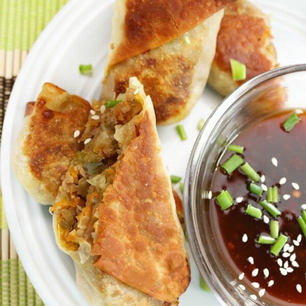 Crispy dumplings on a plate with dipping sauce, garnished with sesame seeds and chopped green onions, reminiscent of an easy egg roll recipe.