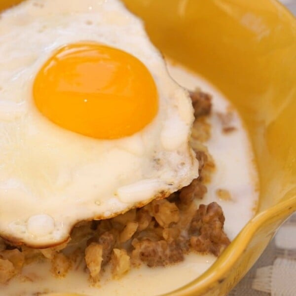 A delicious take on breakfast, this sausage and egg savory oatmeal is topped with a perfectly fried egg with a runny yolk, all served in a vibrant yellow bowl.