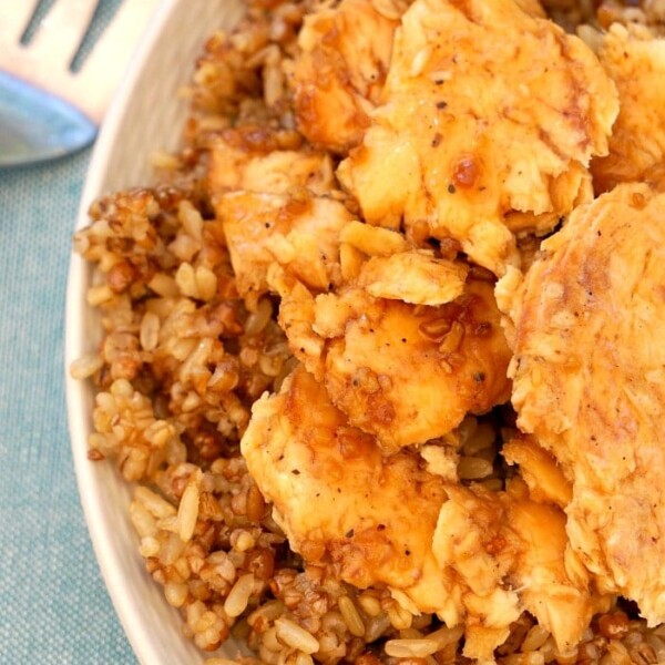 A plate of seasoned chicken pieces on a bed of brown rice, reminiscent of the comforting flavors found in a maple glazed salmon recipe, with a fork on the side.