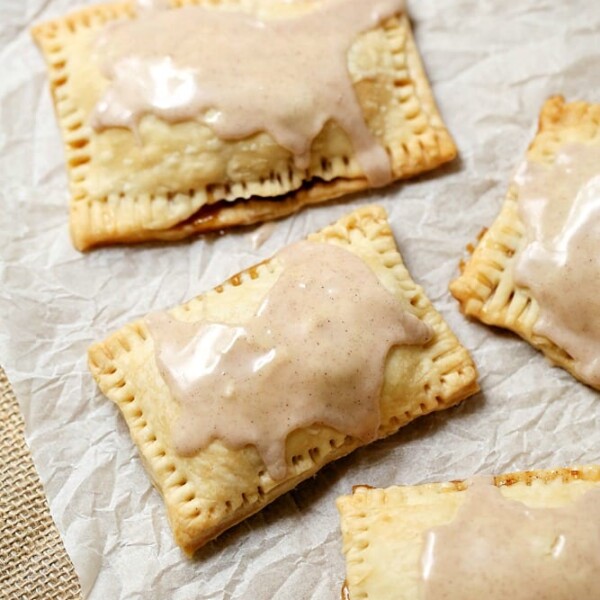 Four homemade pop tarts with icing sit invitingly on parchment paper, promising a delightful treat.