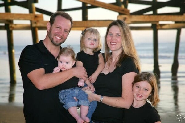 A family of five, celebrating milestones under a beach pier, poses in matching black shirts.